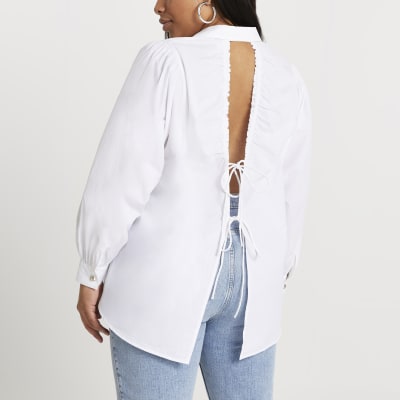 Woman wears white shirt with open back with ties, jeans and silver hoop earring.
